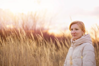 Genç sarışın kadın, batan güneşin altında yalnız başına yürüyor.