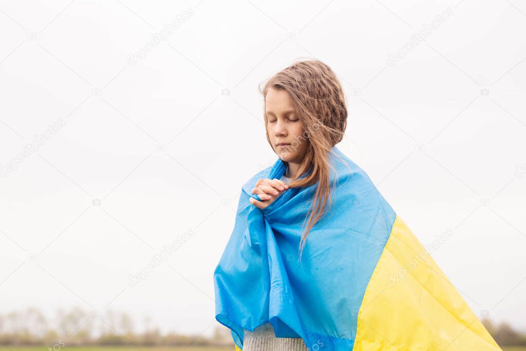 A little girl with the flag of Ukraine prays for the victory of her country