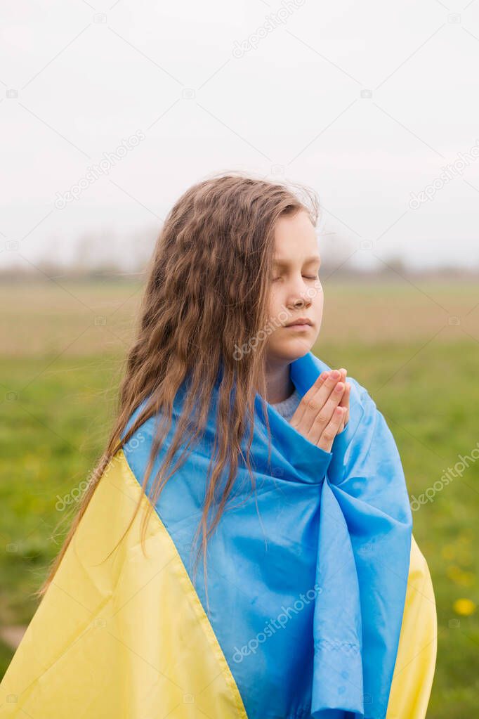 A little girl with the flag of Ukraine prays for the victory of her country