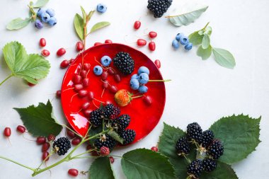 Kırmızı tabakta çeşitli yaz meyveleri, üst manzara.