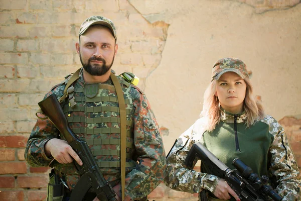 Чоловік і жінка, українські захисники зі зброєю біля зруйнованого будинку під час війни в Україні.