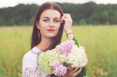 Beautiful young woman with a bouquet of hydrangea in the field