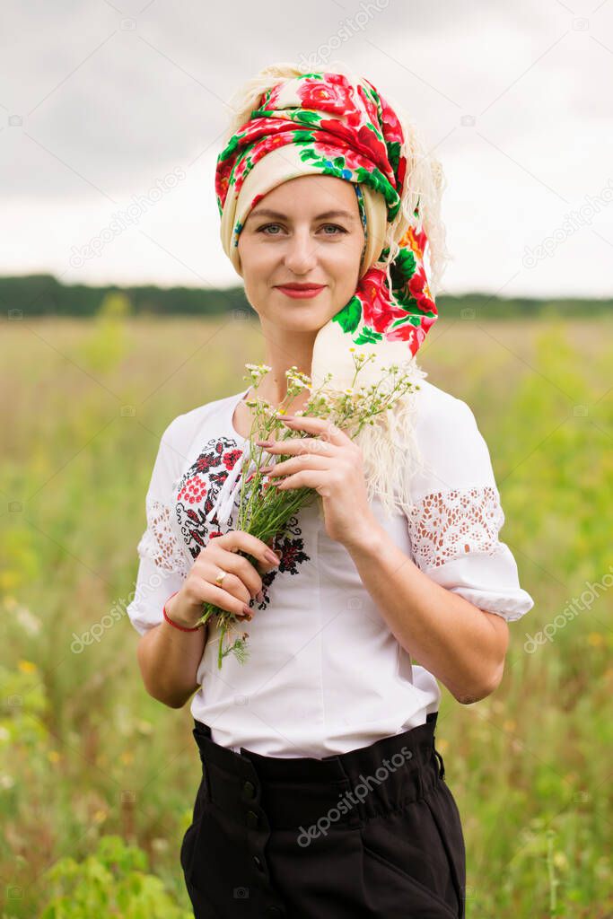 A beautiful Ukrainian woman in a folk dress with a scarf in a field