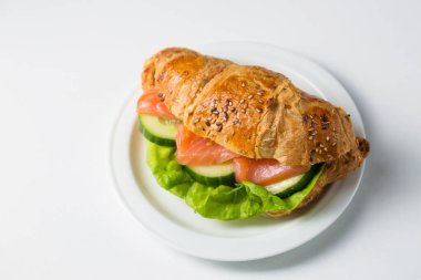 Croissant with salmon and cucumber on a white plate on a white background