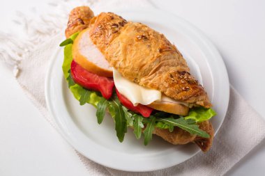 Crispy croissant with ham, cheese and vegetables on a white plate