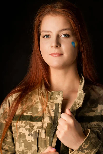 A young woman in camouflage with a blue and yellow heart on her face. Symbol of victory of Ukraine