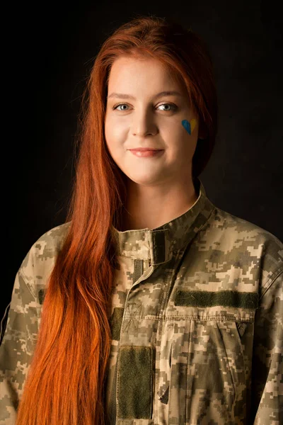 A young woman in camouflage with a blue and yellow heart on her face. Symbol of victory of Ukraine