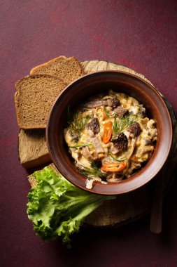 Wild morel mushrooms stewed in sour cream with chili, still life on a burgundy background