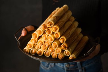 Ruddy crispy tubes with condensed milk on a metal tray in a woman's hands