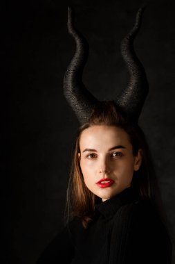 Beautiful young girl with horns on a dark background. Halloween concept