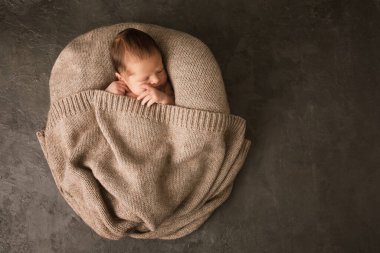 Koyu arkaplanda sıcak örgü örülmüş yeni doğmuş bir bebek.