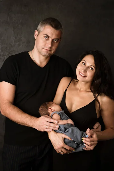 新生児の息子を持つ幸せな若い家族 暗い背景の肖像画 — ストック写真