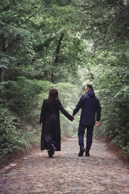 Siyah, vahşi elbiseli bir adam ve bir kız karanlık, sisli bir ormanda yürüyorlar.