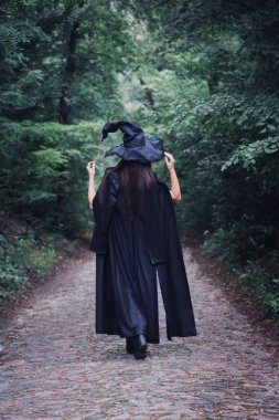 Siyah pelerinli bir cadı ve karanlık bir ormanda büyük siyah bir şapka. Cadılar Bayramı konsepti