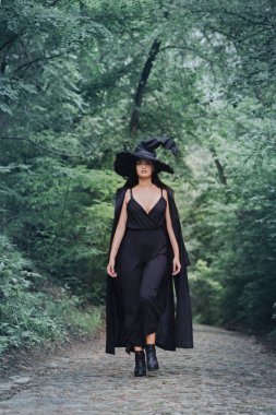 Siyah pelerinli bir cadı ve karanlık bir ormanda büyük siyah bir şapka. Cadılar Bayramı konsepti