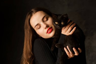 Siyah arka planda siyah kedisi olan hoş bir genç kadın.