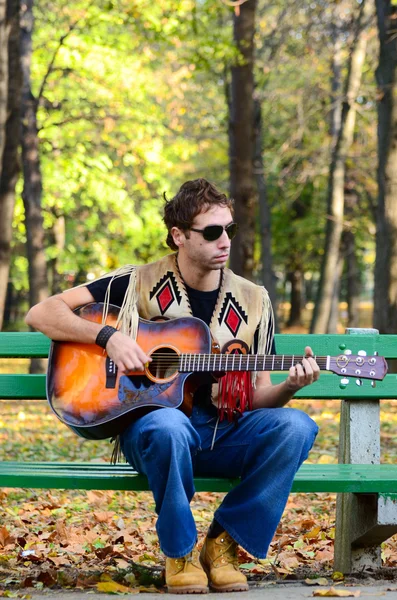 Man playing guitar on bench in park — Stock Photo, Image