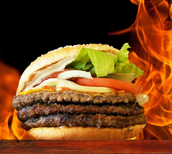 Alev arka plan karşı ahşap plaka üzerinde hamburger — Stok fotoğraf
