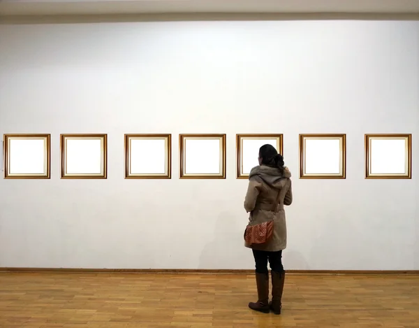 Mulher na sala da galeria olhando para molduras vazias — Fotografia de Stock