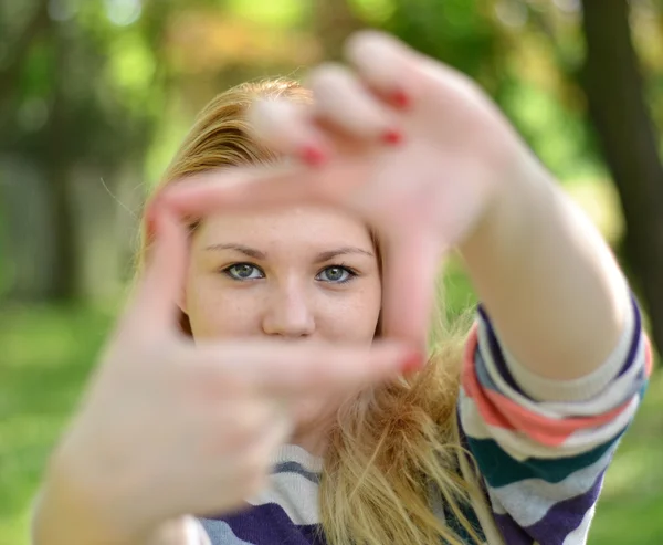 Mooi meisje maken frame met handen terwijl buitenshuis — Stockfoto