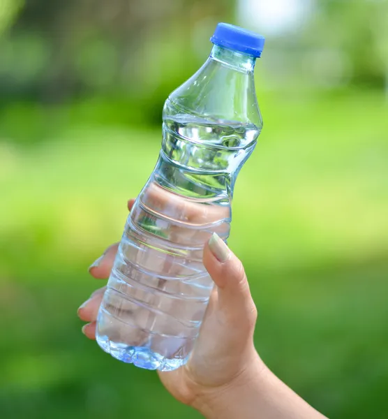 Donna mano tenendo bottiglia d'acqua contro sfondo verde — Foto Stock