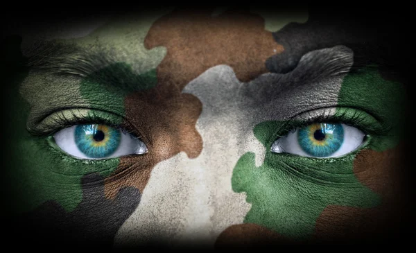 Солдатское лицо с армейскими цветами, смотрящее из темноты — стоковое фото