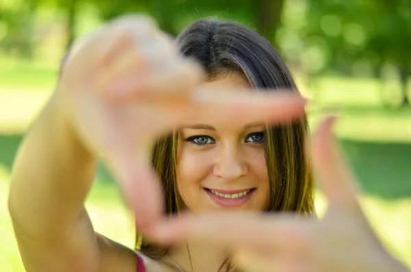 Hermosa chica haciendo marco con las manos mientras está al aire libre — Foto de Stock