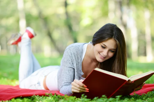Красивая улыбающаяся женщина читает книгу в парке — стоковое фото