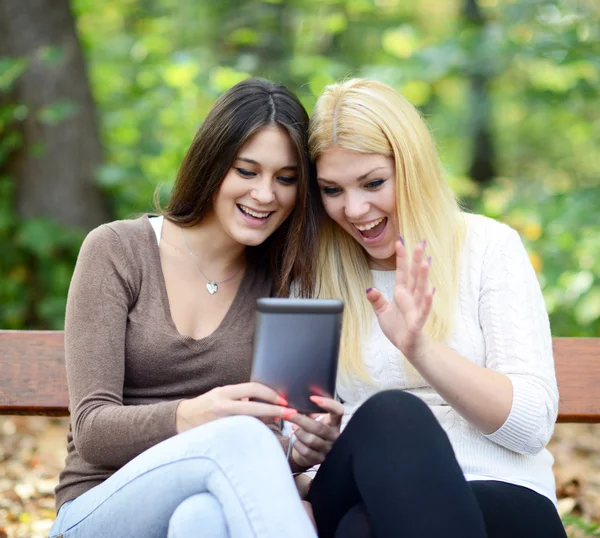 Dos mujeres jóvenes mirando tableta y chating en línea con un amigo — Foto de Stock