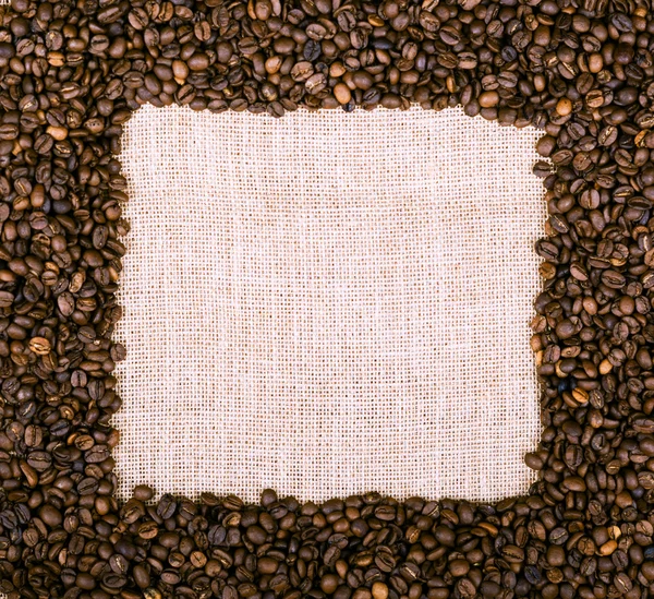 Moldura de grãos de café sobre tecido de serapilheira — Fotografia de Stock