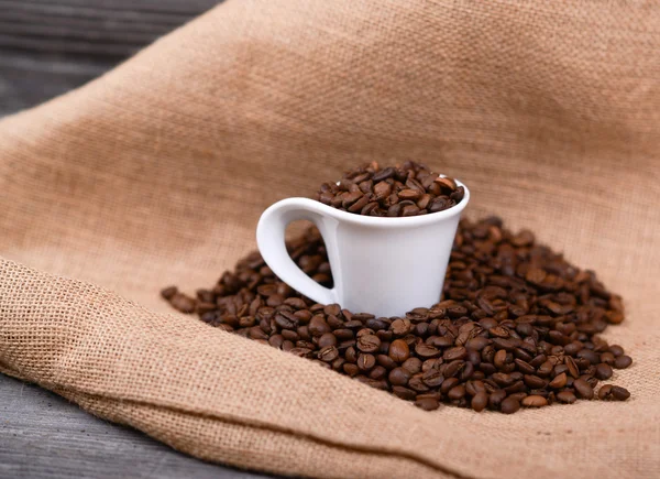 Cup of coffee filled with coffee beans against wooden background — Stock Photo, Image