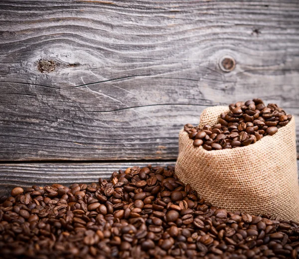 Sack of coffee grains against grunge wooden wall — Stock Photo, Image