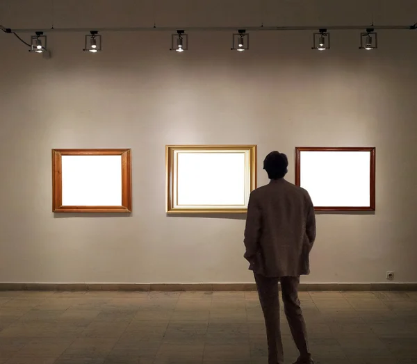 Man in Galerie kamer kijken naar lege afbeeldingsframes — Stockfoto