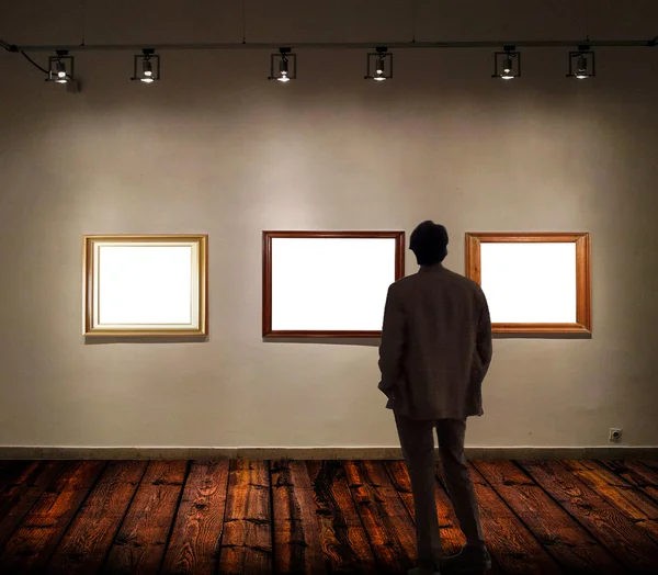 Man in gallery room looking at empty picture frames — Stock Photo, Image