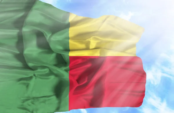 Benin vinker flag mod blå himmel med solstråler - Stock-foto