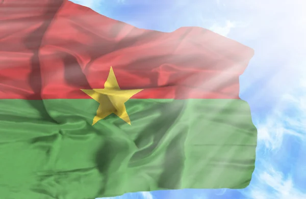 Burkina Faso agitando bandeira contra o céu azul com raios de sol — Fotografia de Stock