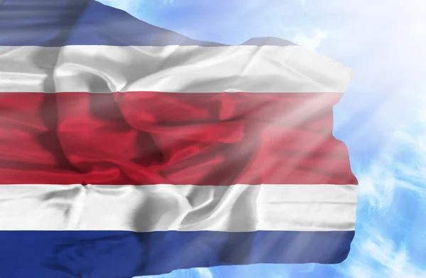 Коста-Рика машет флагом на фоне голубого неба с солнечными лучами — стоковое фото