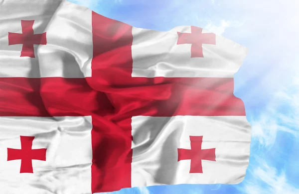 Gruzie mává vlajkou proti modré obloze se slunečními paprsky — Stock fotografie