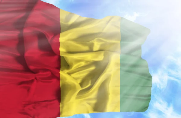 Guinée agitant le drapeau contre le ciel bleu avec des rayons de soleil — Photo