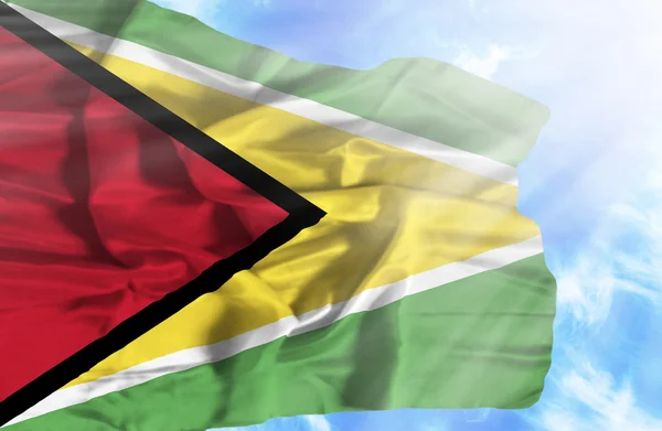 Guyana viftande flagga mot blå himmel med solstrålar — Stockfoto