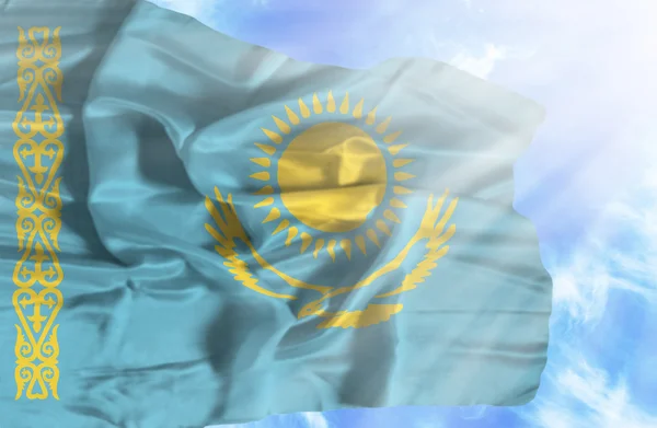 Kasachstan schwenkt Flagge gegen blauen Himmel mit Sonnenstrahlen — Stockfoto