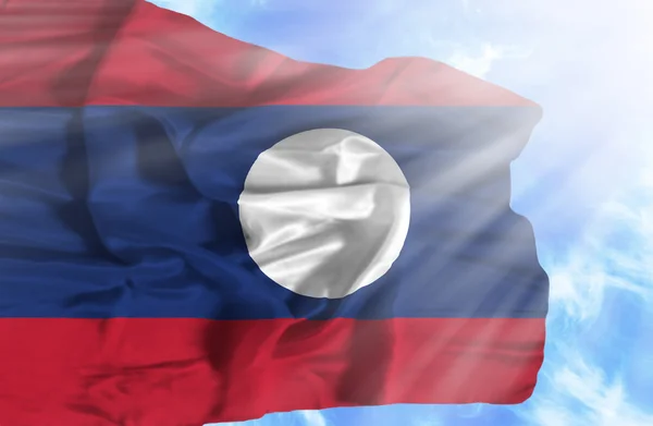 Laos waving flag against blue sky with sunrays — Stock Photo, Image