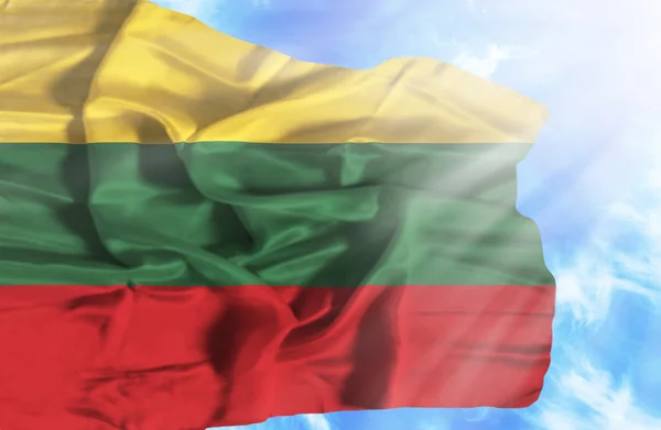 Litva mává vlajkou proti modré obloze se slunečními paprsky — Stock fotografie