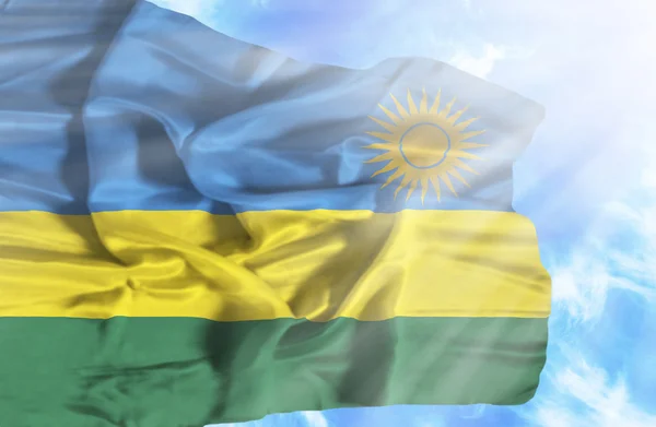 Rwanda zwaaien vlag tegen blauwe hemel met zonnestralen — Stockfoto