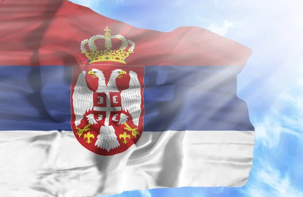 Serbia waving flag against blue sky with sunrays — Stock Photo, Image