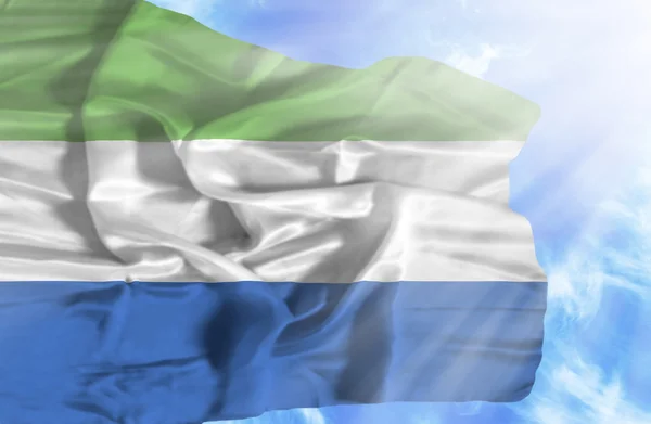 Sierra Leona ondeando bandera contra el cielo azul con rayos de sol —  Fotos de Stock