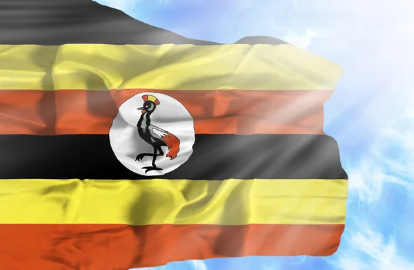 Uganda vinker flag mod blå himmel med solstråler - Stock-foto