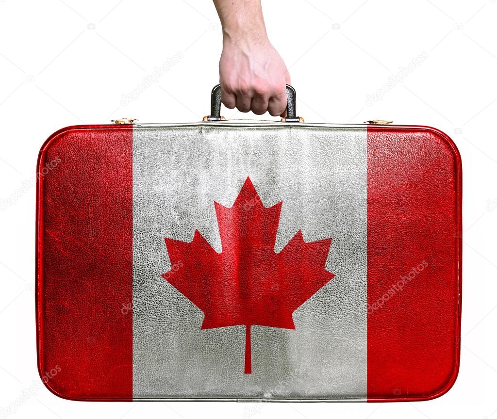 Tourist hand holding vintage leather travel bag with flag of Can