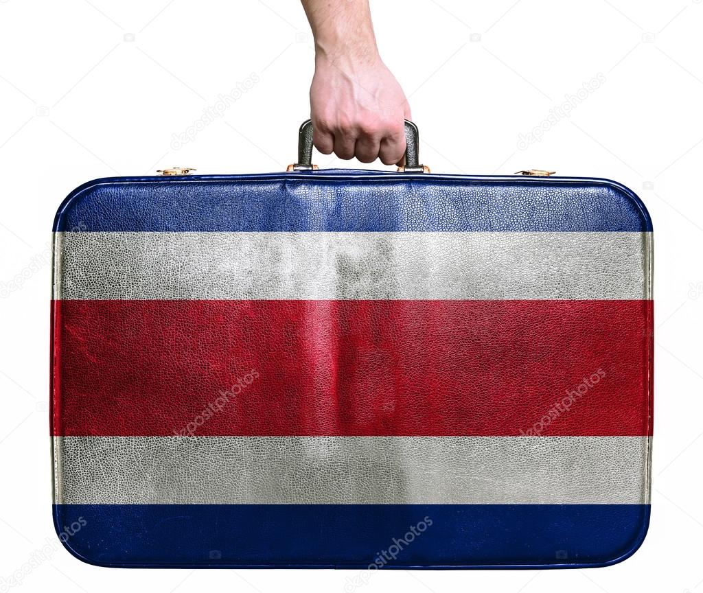 Tourist hand holding vintage leather travel bag with flag of Cos
