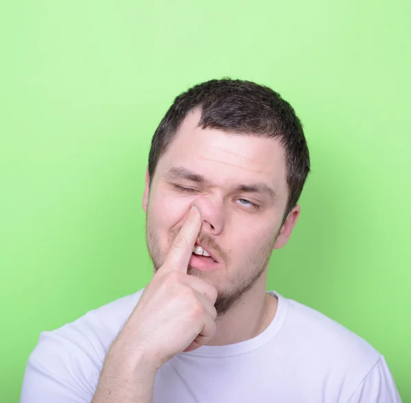 Portrait of a young man with his finger in his nose against gree — Stock Photo, Image